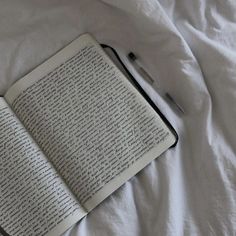 an open book sitting on top of a bed next to a pen