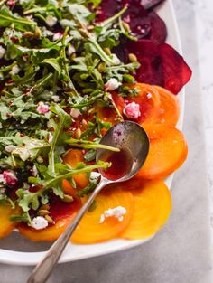 a white plate topped with sliced up beets and other veggies next to a spoon