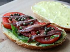 a sandwich with tomatoes and capers on it next to a piece of bread that has been cut in half