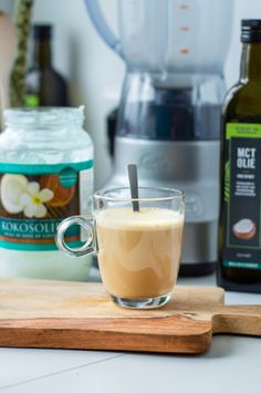 a cup of coffee sitting on top of a wooden cutting board next to an electric blender