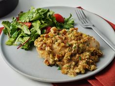 a white plate topped with meat and salad next to a fork on a red napkin