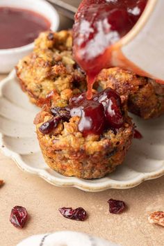 someone pouring sauce on some muffins with cranberry sauce in the background