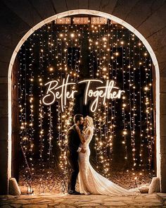 a bride and groom standing in front of an archway with lights on the wall behind them