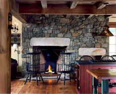 a stone fireplace in the middle of a kitchen with chairs around it and a table next to it