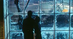 two people standing in front of a window looking out at the snow and trees outside