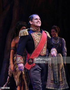 a man dressed in an elaborately decorated uniform stands on stage with other people around him