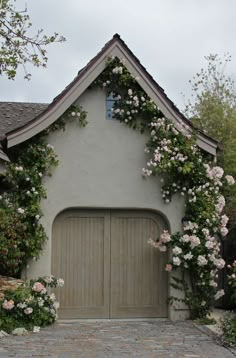 a house with flowers growing on the side of it and a garage door in front