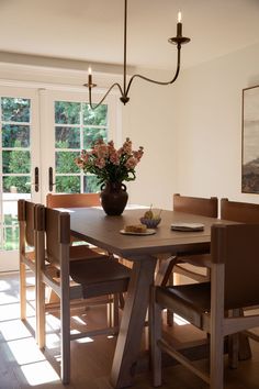 a dining room table with chairs and a vase filled with flowers sitting on top of it