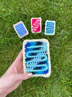 someone is holding up their crocheted phone case in the grass with four pieces of it