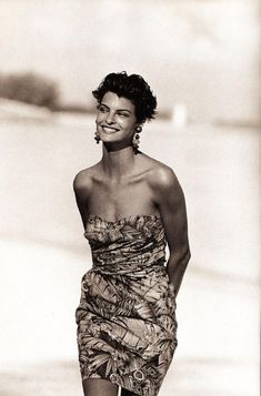 an old photo of a woman walking on the beach wearing a dress and smiling at the camera