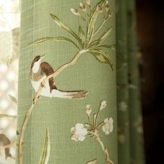 a bird sitting on top of a green curtain next to a flowered window sill