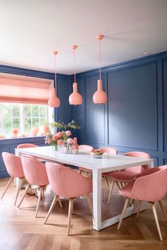 a dining room with blue walls, pink chairs and white table surrounded by pink lamps