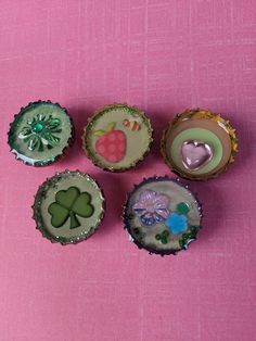 four miniature bottlecaps are sitting on a pink surface with green and white decorations