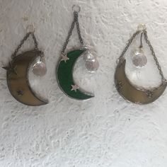 three moon and star charms hanging from chains on a white wall with snow flakes