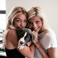 two beautiful young women hugging each other while holding a dog