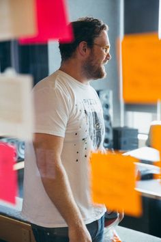 a man standing in front of a table with orange sticky notes on the wall behind him