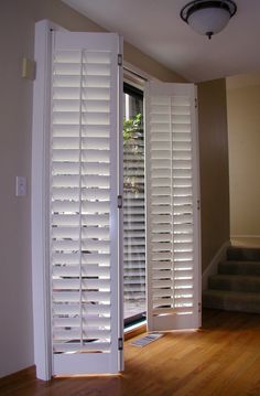 an open window with white shutters and wooden flooring in front of the door