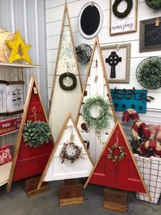 three wooden christmas trees with wreaths hanging on the wall behind them and other holiday decorations