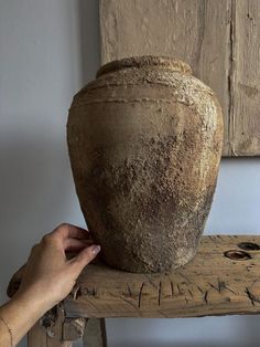 a person holding up a large vase on top of a wooden table