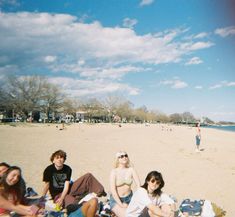 a group of young people sitting on top of a beach next to each other under a blue sky