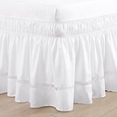 white bed skirt with ruffles on the bottom and side panels, in front of a wooden floor