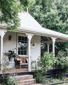 a white house with porch and steps leading up to it's front door, surrounded by greenery