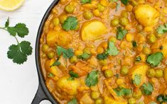 a pan filled with potatoes and peas on top of a white table next to cilantro