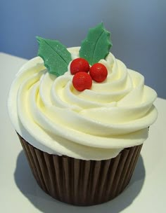 a cupcake with white frosting and topped with holly leaves, red berries and green leaves