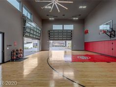 an indoor basketball court with hard wood flooring and red painted doors leading into the gym