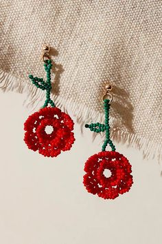 two red beaded earrings hanging from a tasseled piece of fabric on top of a white blanket