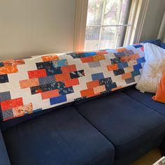 a blue couch with a patchwork quilt on it's back and two pillows