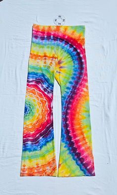 a tie dyed pair of colorful pants hanging on a clothes hanger in front of a white t - shirt