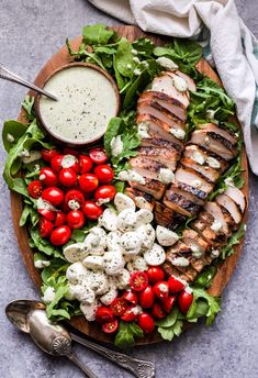 a wooden platter filled with chicken, tomatoes and mozzarella cheeses on top of lettuce