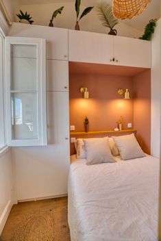 a bed with white linens and pillows in a small room next to a window