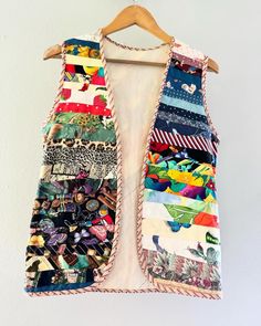 a colorful vest hanging on a white wall next to a wooden hanger filled with fabric