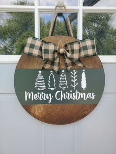 a merry christmas sign hanging on the front door with a bow around it's neck