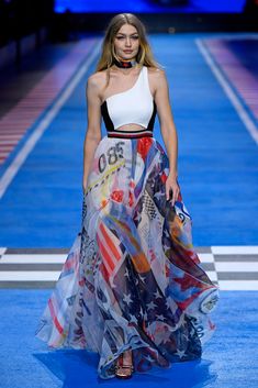 a woman walking down a runway wearing a dress with american flags on the bottom and sides