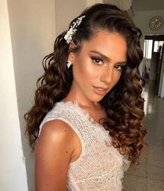 a woman in a white dress with flowers on her head and long curly hair is posing for the camera