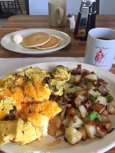 an omelet with eggs, potatoes and pancakes on a plate next to a cup of coffee