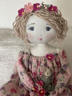 the doll is wearing a pink dress with flowers in her hair and holding a teddy bear