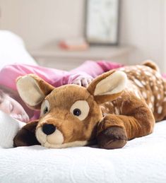 a stuffed deer laying on top of a bed next to a baby sleeping in it's arms