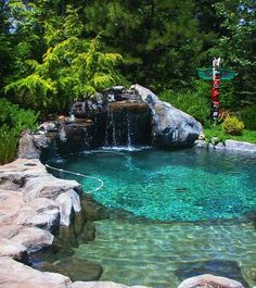 an outdoor swimming pool surrounded by rocks and water features a waterfall that flows into the pond