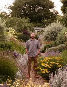 a man standing in the middle of a garden filled with lots of plants and flowers