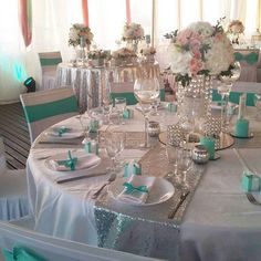 the table is set with silver and aqua colored napkins, plates, cups, and vases