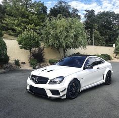 a white mercedes cla is parked in the parking lot next to some bushes and trees