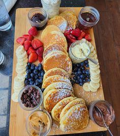 a wooden cutting board topped with pancakes covered in powdered sugar next to fruit and dips