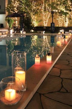 lighted candles are lined up along the edge of a swimming pool