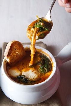 a spoonful of soup is being lifted from a white bowl with bread on the side