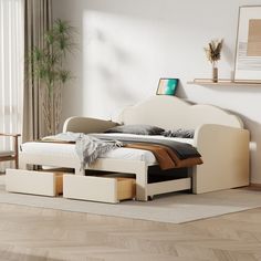 a white bed with drawers underneath it in a living room next to a large window