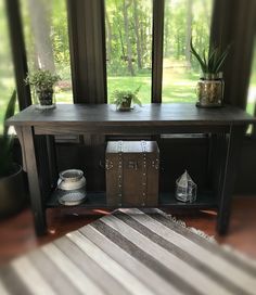 a wooden table with a trunk on it in front of a window and potted plants